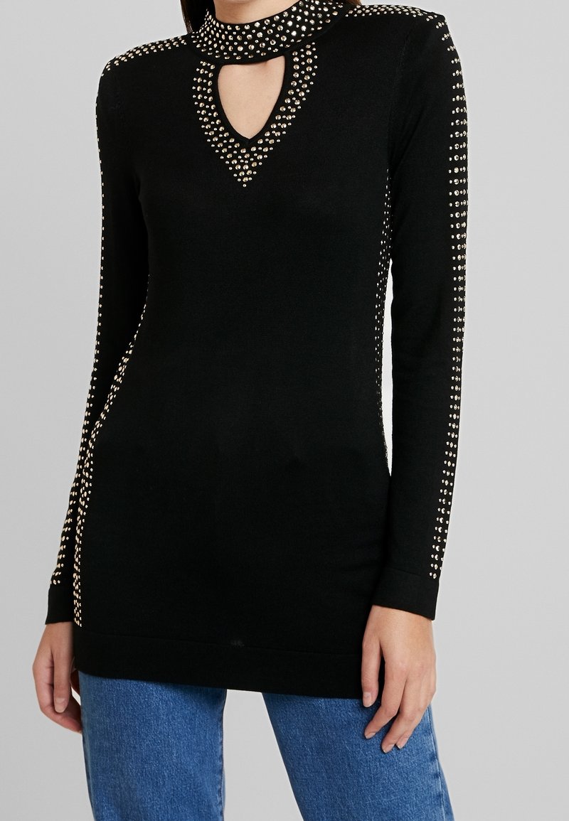 Top negro de manga larga con escote en forma de llave, adornado con tachuelas doradas a lo largo del cuello y los lados; material de punto suave.
