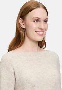 Hellbeige Strickpullover mit weitem Bootsausschnitt und subtiler Textur. Verfügt über kleine, glitzernde Akzente im gesamten Stoff.