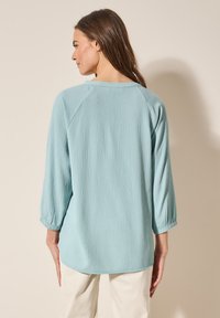 Maglietta a manica lunga azzurro chiaro con tessuto testurizzato, scollatura rotonda e vestibilità rilassata. Presenta maniche 3/4 e orlo curvo.