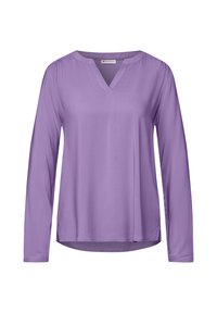 Blusa de manga larga en color lavanda con escote en V y dobladillo ligeramente curvado. Hecha de una tela suave con un brillo sutil y detalles fruncidos en los hombros.