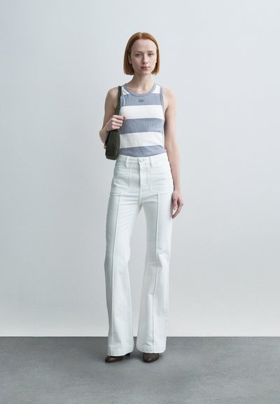 Haut sans manches rayé bleu et blanc ; jean blanc évasé taille haute ; petit sac à bandoulière vert foncé ; modèle portant des talons marron.