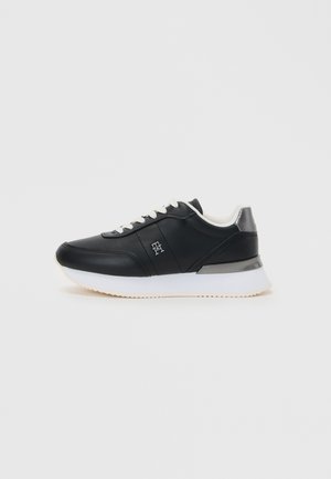 Black synthetic sneakers with white sole, round toe, lace-up design, and silver accent on the heel. Smooth texture and minimalistic style.