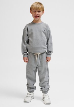 Grijze sweatshirt en bijpassende trainingsbroek met elastische boorden, met een klein embleem op de borst en een verstelbare tailleband. Witte sneakers.