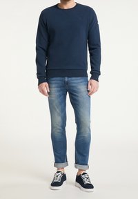 Tmavě modrá mikina s kulatým výstřihem, žebrovanými manžetami a lemem; v kombinaci se světle modrými džíny a tmavými teniskami s bílými tkaničkami.