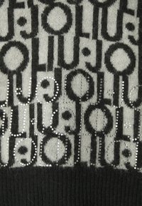 Maglione lavorato a maglia caratterizzato da un motivo grigio e nero con dettagli metallici, che presenta forme circolari e lineari, una texture morbida e orlo a coste.