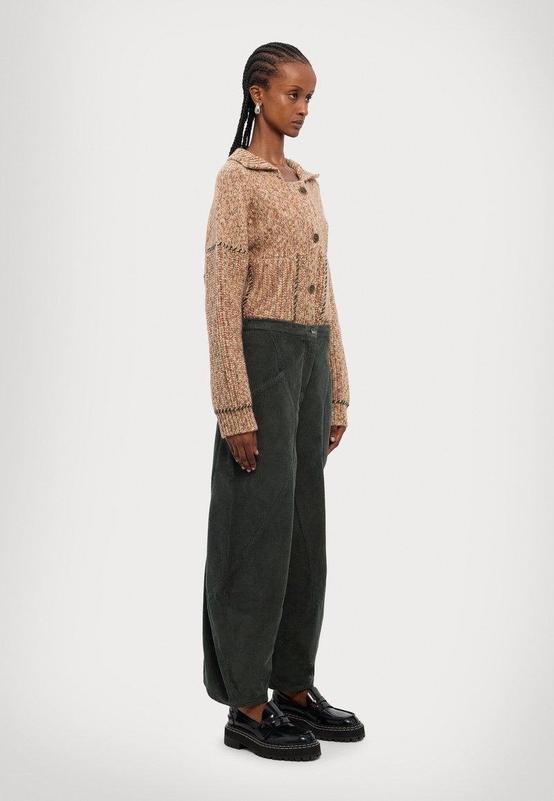 Strikket, beige cardigan med krave og knapper, parret med mørkegrønne fløjl bukser. Sorte platform loafers fuldender outfittet.