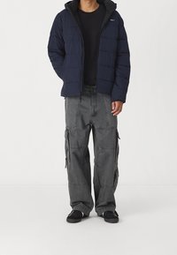 Marineblå dynejakke med hætte, kombineret med løse grå cargobukser med flere lommer og sorte sneakers.