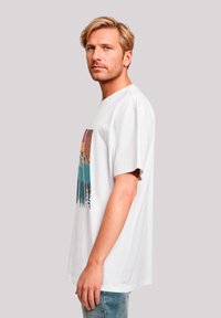 Witte katoenen T-shirt met een kleurrijke grafische print van bergen en bomen. Luchtige pasvorm met korte mouwen, ronde halslijn en zachte textuur.