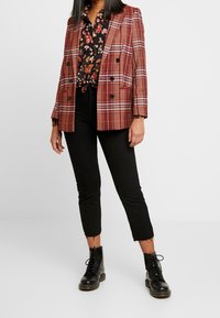 Red and beige plaid blazer with double-breasted buttons, paired with a black floral shirt, black cropped pants, and lace-up black boots.