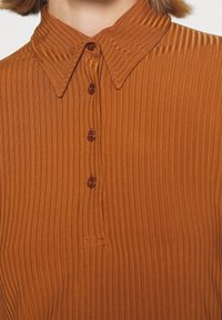 Rust-colored collared shirt with vertical ribbed texture, featuring a half-placket with brown buttons and pointed collar.