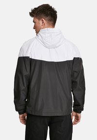Veste légère en noir et blanc avec capuche, présentant un design coloré et des poignets élastiques. Texture lisse et coupe ample.
