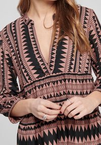 Long-sleeve dress featuring a deep V-neck, black and dusty pink geometric patterns, textured fabric, and gathered cuffs at the sleeves.