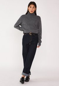Maglione grigio con collo a lupetto e polsini a costine abbinato a jeans blu scuro a vita alta con orli arrotolati e una cintura nera con fibbia rotonda.