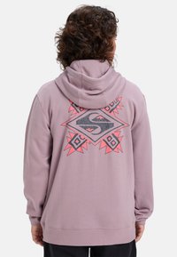 Sudadera morada con un gran diseño gráfico en la espalda que presenta formas geométricas y acentos en rosa contrastante. Tela suave, mangas largas.
