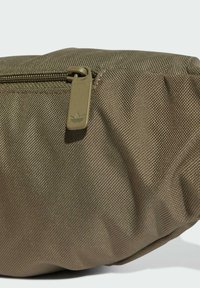 Bolsa de tela verde oliva con una superficie texturizada y cierre de cremallera con una lengüeta beige que muestra un logo. Forma redondeada.