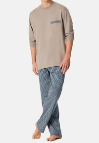 Beige overhemd met lange mouwen en borstzak, en blauwe pyjamabroek met geometrische patronen. Zachte katoenen stof, ontspannen pasvorm.