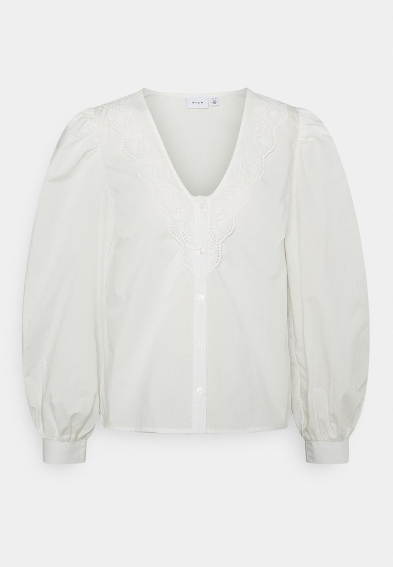 Blusa branca com decote em V, mangas bufantes e detalhes em renda ao longo da gola. Apresenta um fechamento por botões na parte da frente. Textura suave.