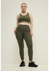 Olivengroene sportbh met een textuurband, gecombineerd met bijpassende leggings. De stof is glad, met een aansluitend ontwerp, zijknaden en contourdetails.