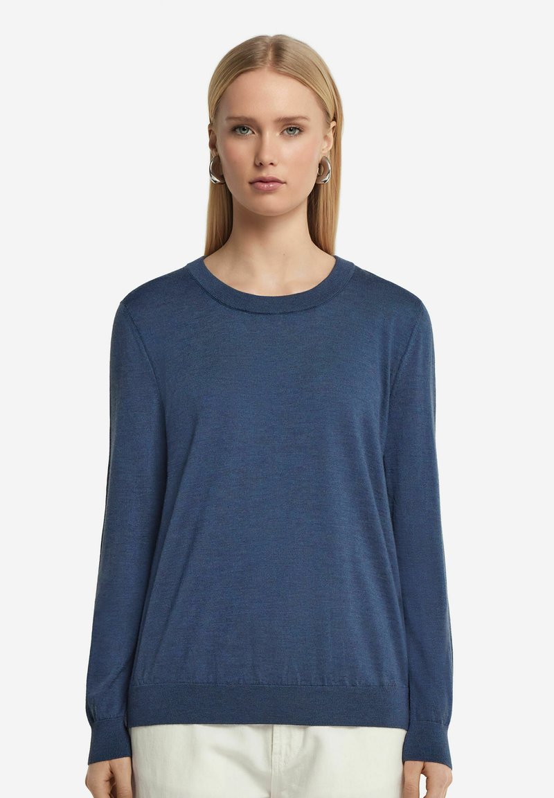 Niebieski sweter z długim rękawem, wykonany z dzianiny, z okrągłym dekoltem, miękką teksturą, ściągaczami przy mankietach i luźnym krojem, w połączeniu z jasnymi spodniami.