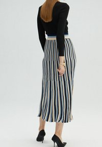 Jupe midi rayée avec des lignes verticales bleues, beiges et crème, fabriquée dans un tissu doux ; présente une taille ajustée et un ourlet évasé.