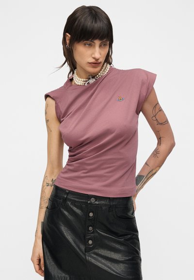 Lyhythihainen, vartalonmyötäinen t-paita vaaleanpunaisessa mauven sävyssä, jossa on kierretty muotoilu ja pieni kirjailtu yksityiskohta. Yhdistetty mustaan nahkahameeseen.