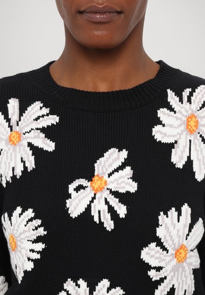 Schwarzer Strickpullover mit weißen Gänseblümchen und orangefarbenen Zentren. Das Design umfasst einen gerippten Rundhalsausschnitt und eine strukturierte Stoffqualität.