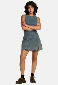 Denim-mekko, vaaleansininen, ilman hihoja, sivuaukolla, erottuva tikkaus, tiukka siluetti, yhdistettynä ruskeisiin kenkiin ja mustiin sukkiin.