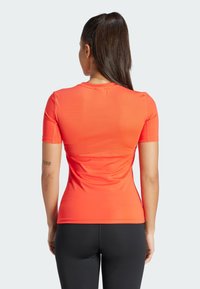 Camiseta atlética de manga corta en naranja brillante, hecha de una tela suave y elástica. Presenta un escote redondo y un diseño ajustado.