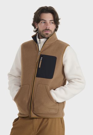 Chaleco de forro polar en marrón, con un bolsillo negro con cremallera, dos bolsillos frontales y un cuello alzado. El interior es de color crema.