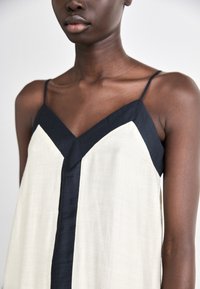 Sidenlinne med V-ringning, i krämfärgad kropp och marinblå detaljer. Tunna axelband och en lätt, slät textur som förbättrar dess flöde.