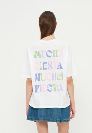 Personne aux longs cheveux bruns portant un t-shirt blanc avec un texte coloré "Mucha Siesta Mucha Fiesta" et une jupe en jean bleue, vue de dos.