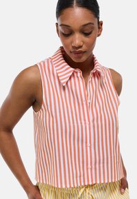 Chemise sans manches à col, à rayures verticales orange et blanches, avec des boutons sur le devant et une coupe courte. Matériau en coton doux.
