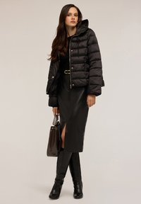 Giacca a vento nera con cappuccio, chiusura con zip e design trapuntato. La gonna è in morbido pelle nera con uno spacco frontale. Gli accessori includono una borsa marrone.