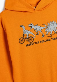 Oranje hoodie met een dinosaurustekening op een fiets, met de tekst "FREESTYLE ROLLING TIME." Zachte katoenen stof, casual ontwerp.