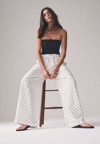 Črni top brez naramnic, kombiniran z belimi hlačami z ohlapno obliko in pikami. Obleka ima pas z vrvico in je nošena s črnimi ravnimi sandali.