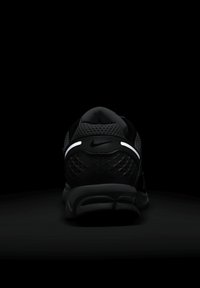 Črne športne čevlje z mrežasto zgornjo površino z teksturo, podloženim petnim delom in odsevnimi belimi poudarki, ki imajo na hrbtni strani obliko diamantnega vzorca.