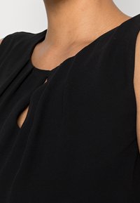 Top senza maniche nero con scollatura rotonda e dettaglio a occhiello, tessuto texturizzato e vestibilità rilassata.