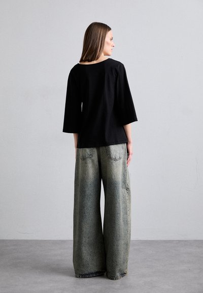 Black, loose-fitting top with elbow-length sleeves paired with oversized, faded, light blue jeans featuring a straight cut and back pockets.