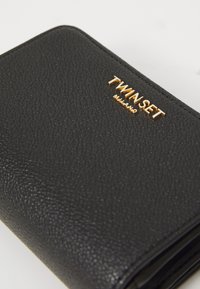 Black textured leather wallet with gold "TWINSET MILANO" branding. Compact design, smooth edges, and glossy accents.