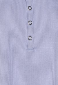 Ljust lila, texturerad tyg med ett våffelmönster; har ett plagg med fyra metallknappar ner i mitten.