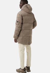 Puffer jacket in light brown with a hood, zippered pockets, and elastic cuffs; paired with cream pants and brown sneakers.