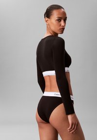 Black long-sleeve top and matching waistband underwear. Features white elastic band with "Calvin Klein" logo. Soft, stretchy fabric.