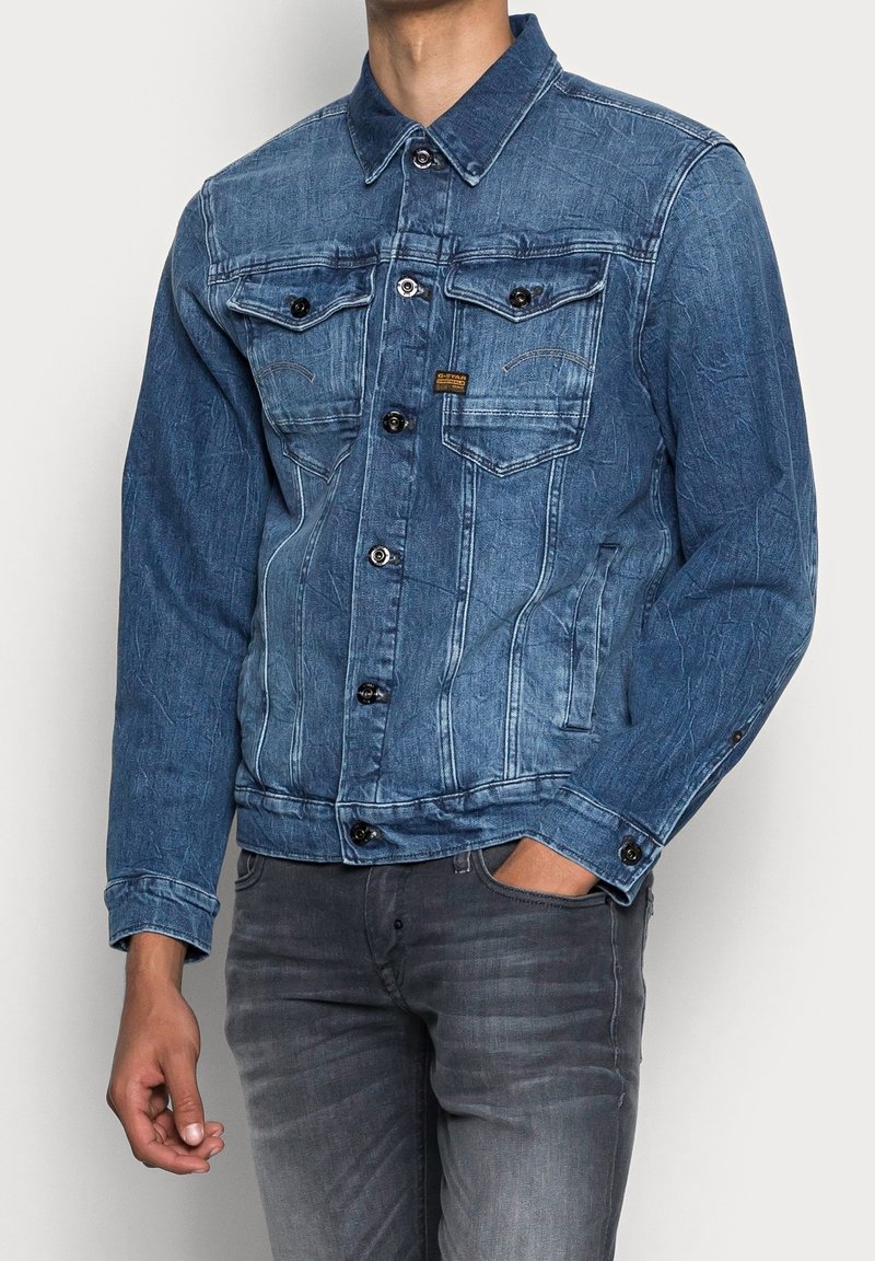 Chaqueta de denim en azul claro con un acabado texturizado, que cuenta con cierre de botones, dos bolsillos en el pecho y mangas largas.