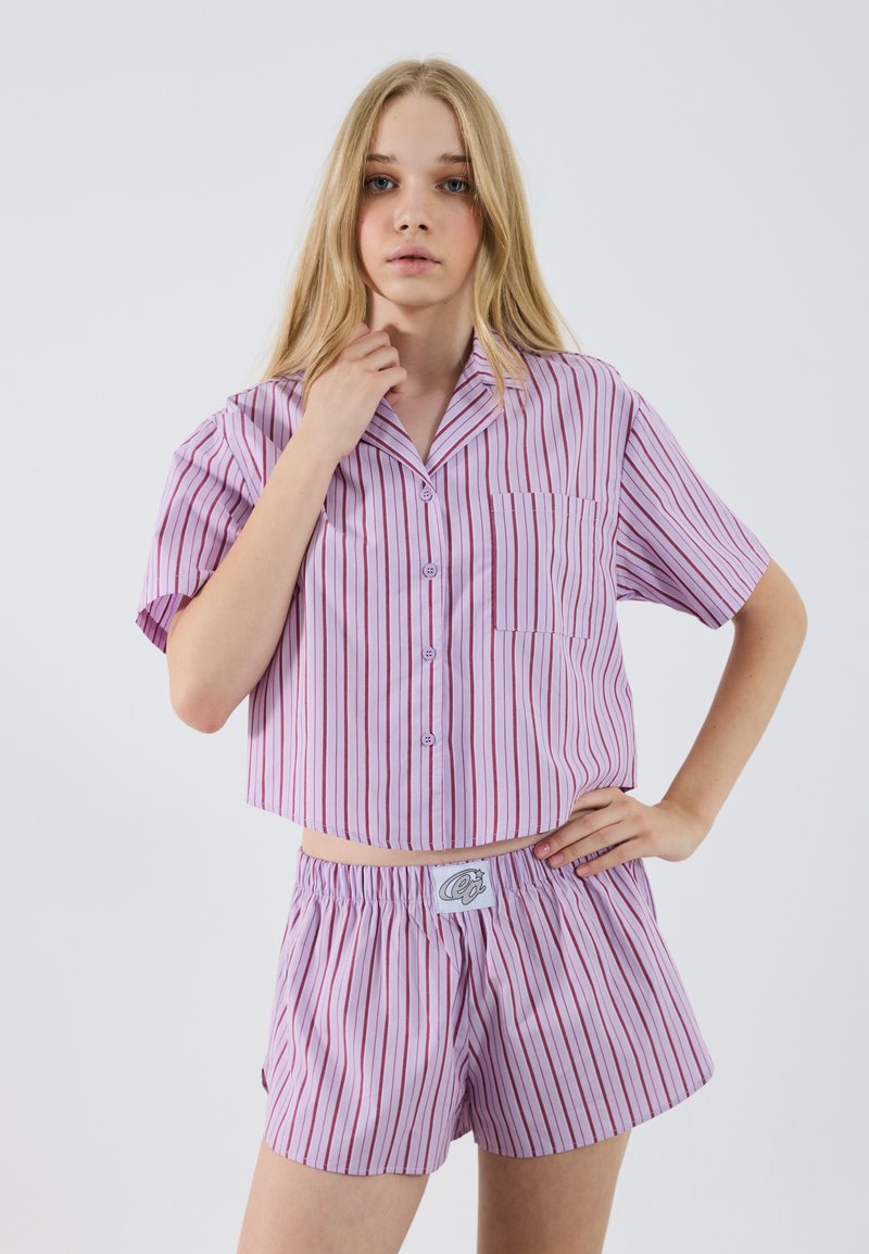Set di pigiama corto a maniche corte di colore lilla chiaro con strisce rosa scuro. Include una camicia con bottoni e tasca, e pantaloni shorts con vita elastica.