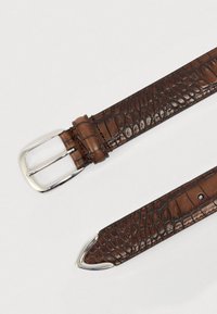 Cinturón de cuero marrón con textura de cocodrilo, hebilla rectangular plateada y punta puntiaguda, con costuras prominentes y orificios para ajuste.