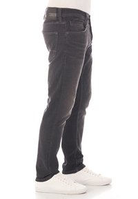 Jeans de mezclilla negra con un corte ajustado, que cuentan con cinco bolsillos y un ligero desgaste. Llevados con zapatillas blancas para un contraste.