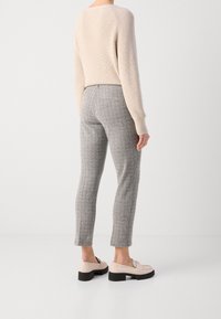 Beige geribbelde trui, grijze textuurbroek met hoge taille, en lichte loafers met een zwarte zool, gezien vanuit de achterkant.