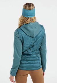 Turkio žalio izoliuoto švarkelio su gobtuvu, turinčio kvadratinius raštus ir grublėtą audinį ant rankovių, derinamo su atitinkamu galvos juosta.