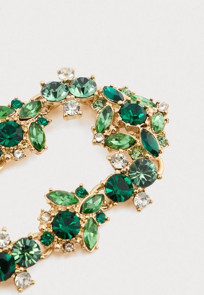 Kultainen rintaneula, jossa on klusteroituja vihreitä ja kirkas kiviä pyöreissä ja marquise-muodoissa valkoista taustaa vasten.
