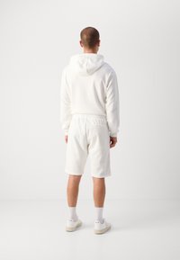 Hvit vevd hettegenser med hette og matchende shorts. Glatt tekstur, avslappet passform. Fullført med hvite sneakers og ankelhøye sokker.